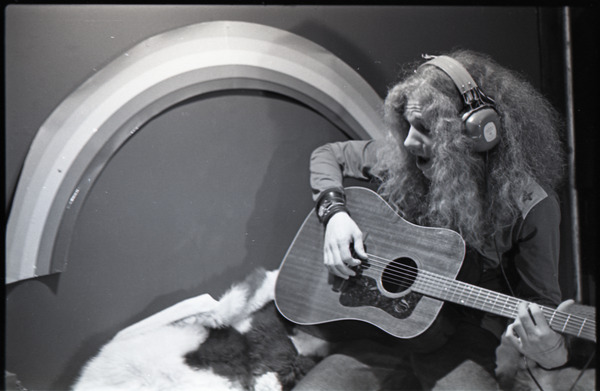 Richie Miller singing and playing guitar, modeling Koss headphones, ca. 1973