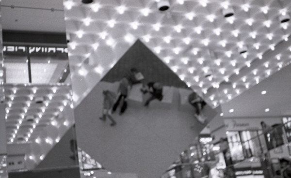 Commune member distributing Free Spirit Press in an indoor shopping mall:             image of magazine distributors in reflection, ca. September 11, 1972